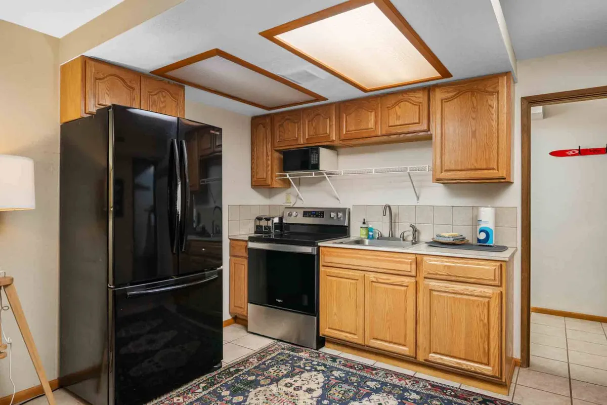 This kitchen scene features a black refrigerator, stainless steel stove, and wooden cabinetry, complemented by a colorful area rug. The layout is functional and cozy, suggesting a separate, well-equipped cooking area that could serve as the basement studio kitchen mentioned in the section.