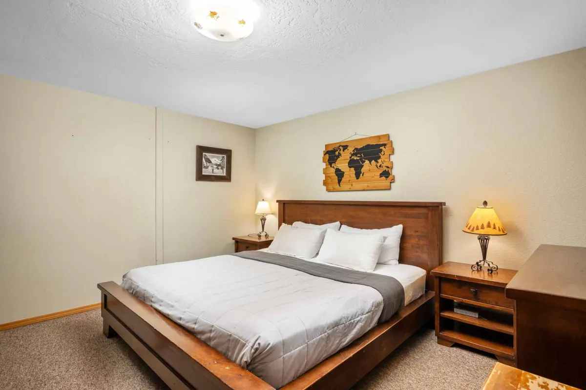 A serene bedroom with a comfortable bed, world map decor above the headboard, nightstand lamps, and a framed picture, evoking a sense of calm and inspiration. The room’s mood is inviting and ideal for quiet reflection or unwinding after a day of adventure.