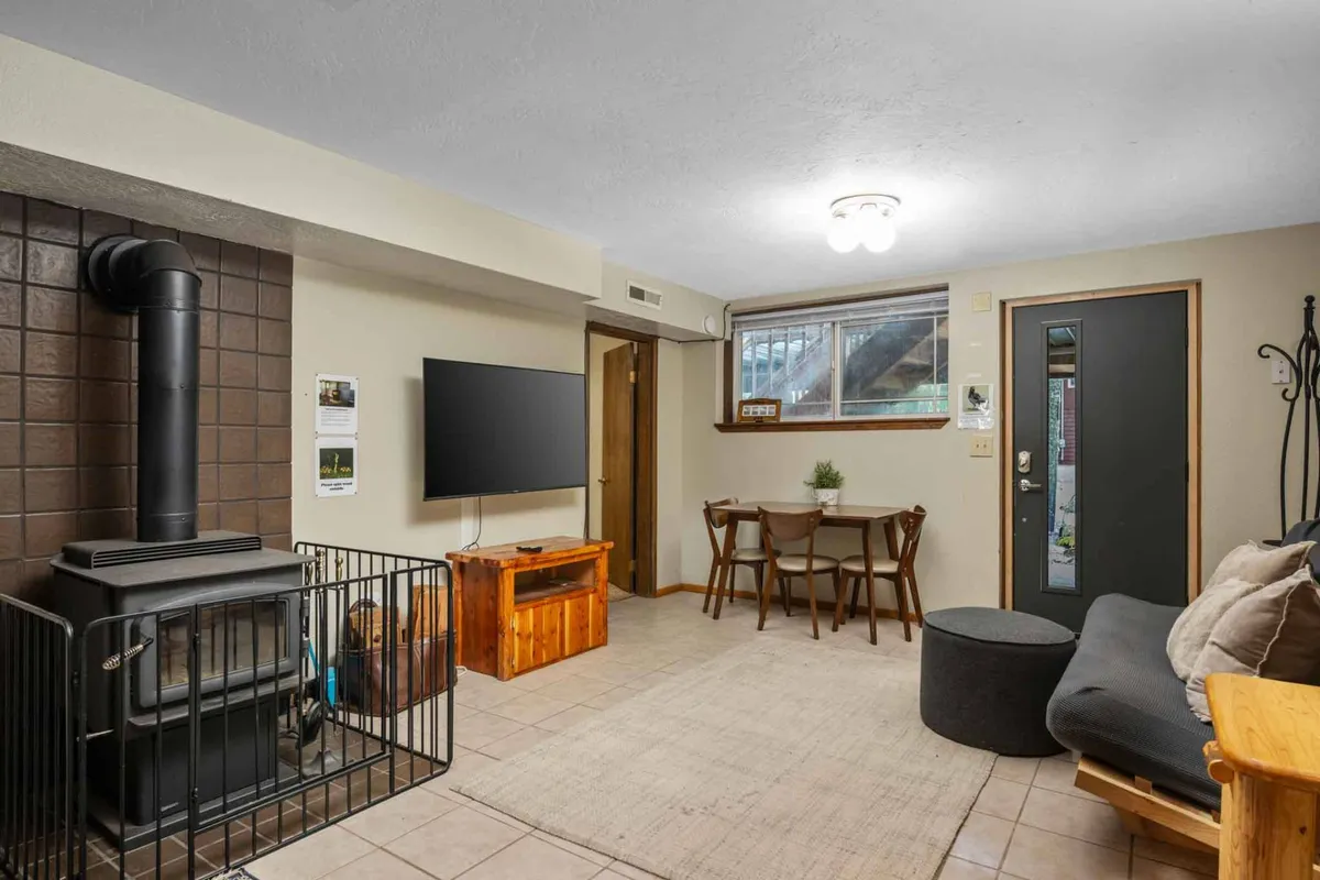 A multi-use communal zone featuring a wood stove, a comfortable sofa, a dining table set for meals or games, and a TV for movie nights. The space is designed for both relaxation and entertainment, with a casual layout that invites guests to gather and unwind.