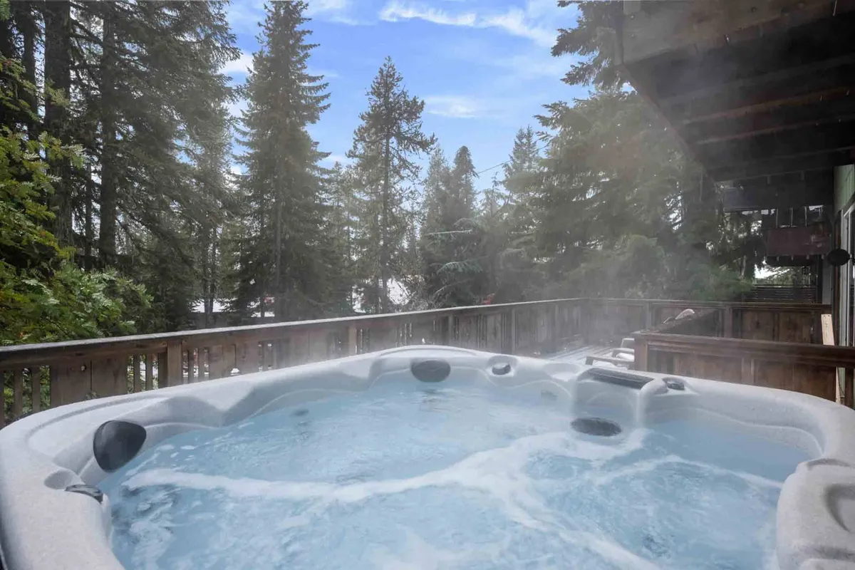 A tranquil deck scene with a private hot tub surrounded by lush trees. The hot tub is the central feature, offering an enticing spot for stargazing or soaking after outdoor adventures. The spacious deck provides enough room for socializing, with views that immerse guests in nature.