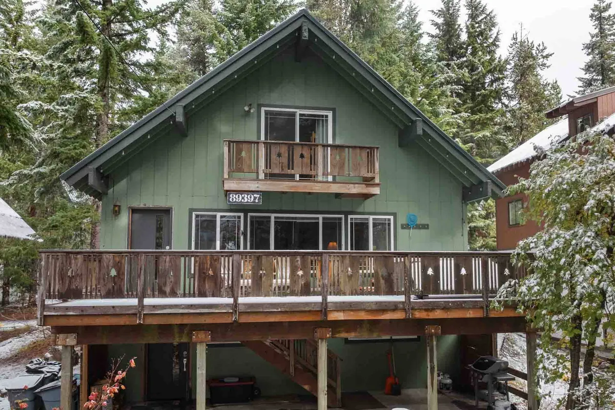 This exterior shot shows the chalet’s wooden balcony and green exterior surrounded by trees. The scene is tranquil and welcoming, suggesting easy access to nature, whether snow-covered or green in summer.