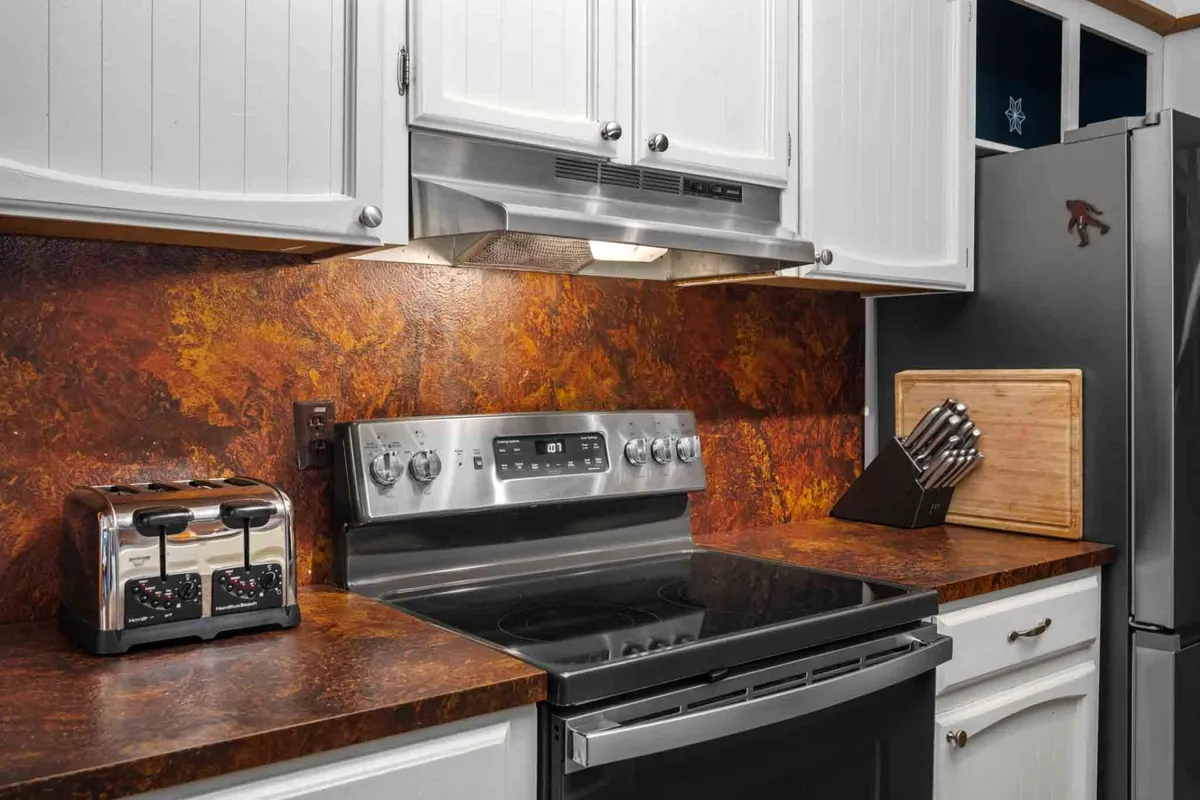 Here, a close-up view of a stainless steel stove, countertop, toaster, cutting board, and knife set creates a homey atmosphere. The setting feels perfect for cooking and baking with loved ones, highlighting the functional and inviting nature of the kitchen spaces.